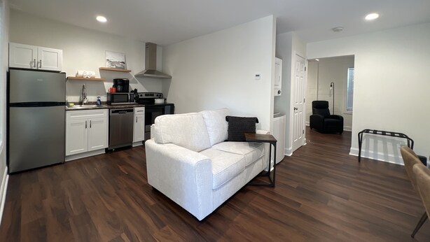 A modern apartment with a kitchen, a white sofa, a dining area, and a black chair. - 1BR Near DT & Mountain Goat Cafe (Greenville)