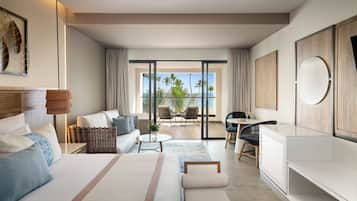 A modern hotel room with a large bed, a sitting area with a sofa and chairs, a dining table, and a view of palm trees and the ocean.