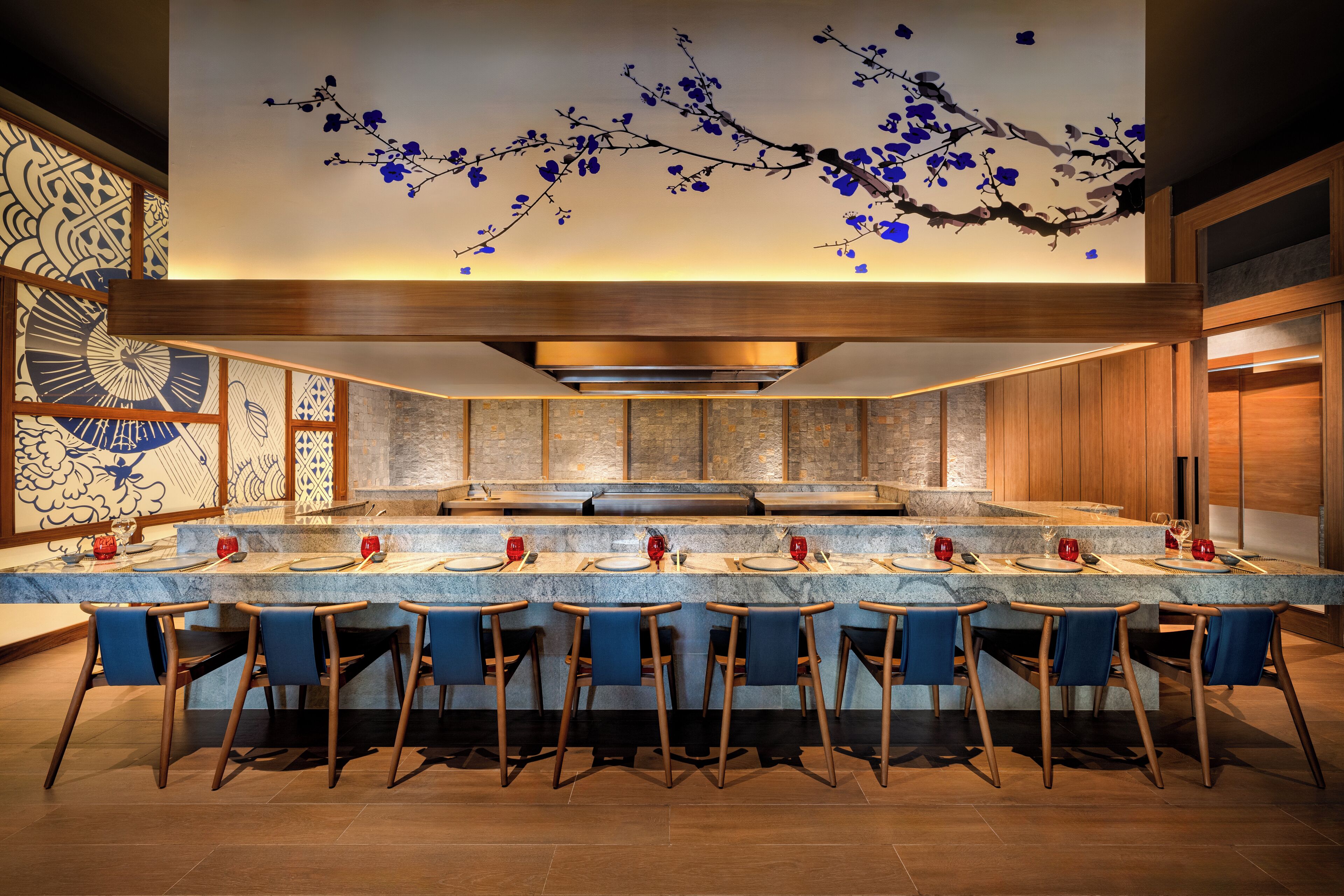A modern bar area with a long counter, multiple stools, and a decorative ceiling with blue floral patterns.