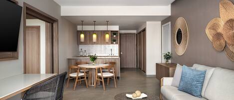 A modern living room with a sofa, a dining table with chairs, a kitchen area with pendant lights, and a large mirror on the wall.