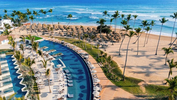 Vista aérea de un resort con una piscina grande, zona de playa y palmeras.