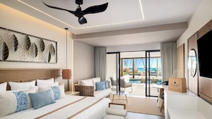 Habitación de hotel moderna con una cama grande, un sofá, un comedor y vista al océano.