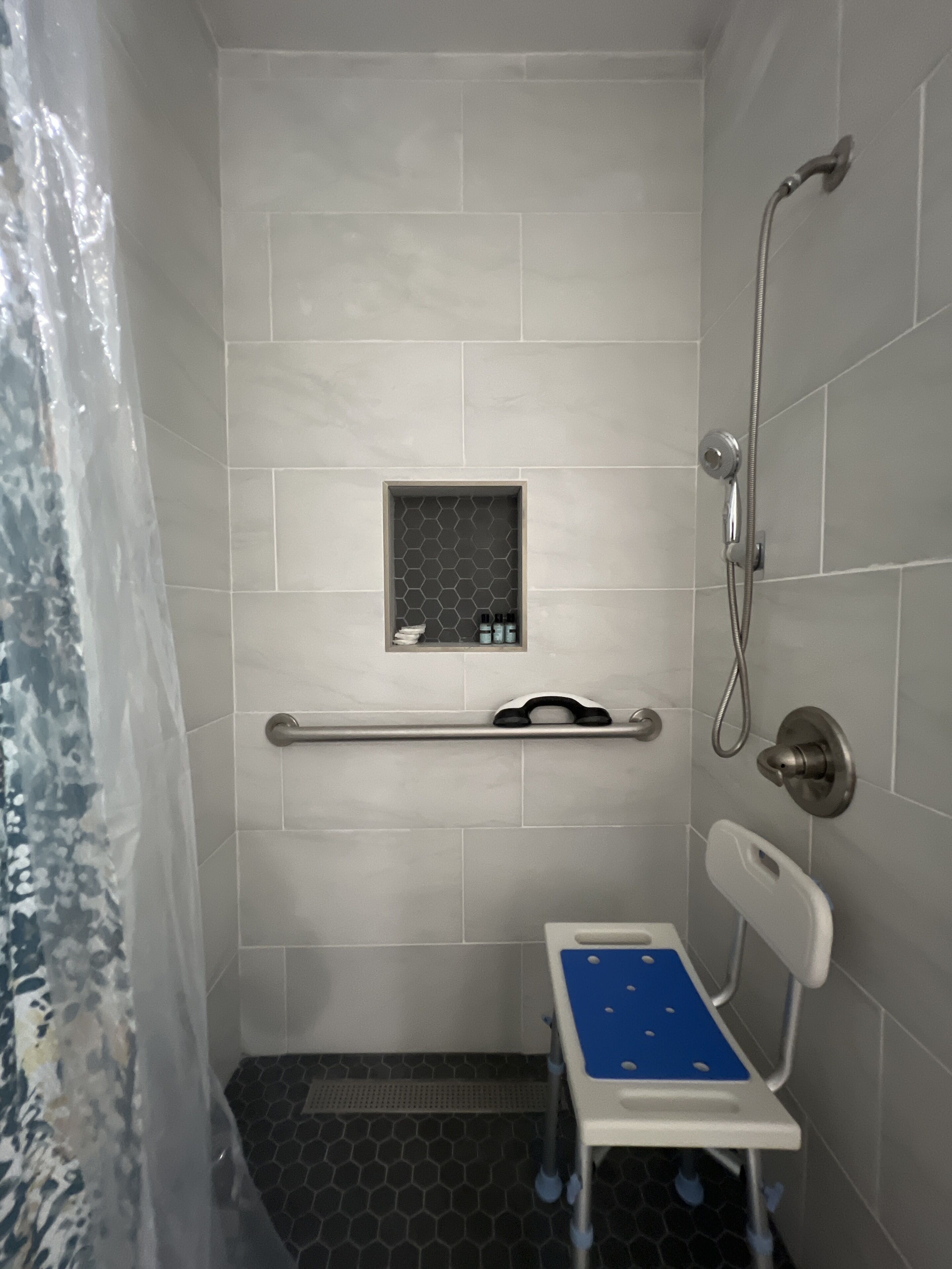 A bathroom with a shower, a toilet with a blue seat, and a grab bar.