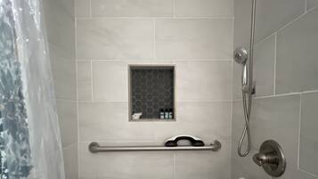 A bathroom with a shower, a toilet with a blue seat, and a grab bar.