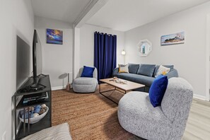 A modern living room with a flat-screen TV, grey and blue upholstered seating, a coffee table, and a decorative bowl on a black side table.