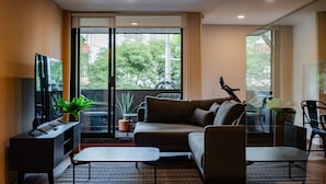 A modern living room with a sofa, a coffee table, a TV, and a balcony with a bicycle.