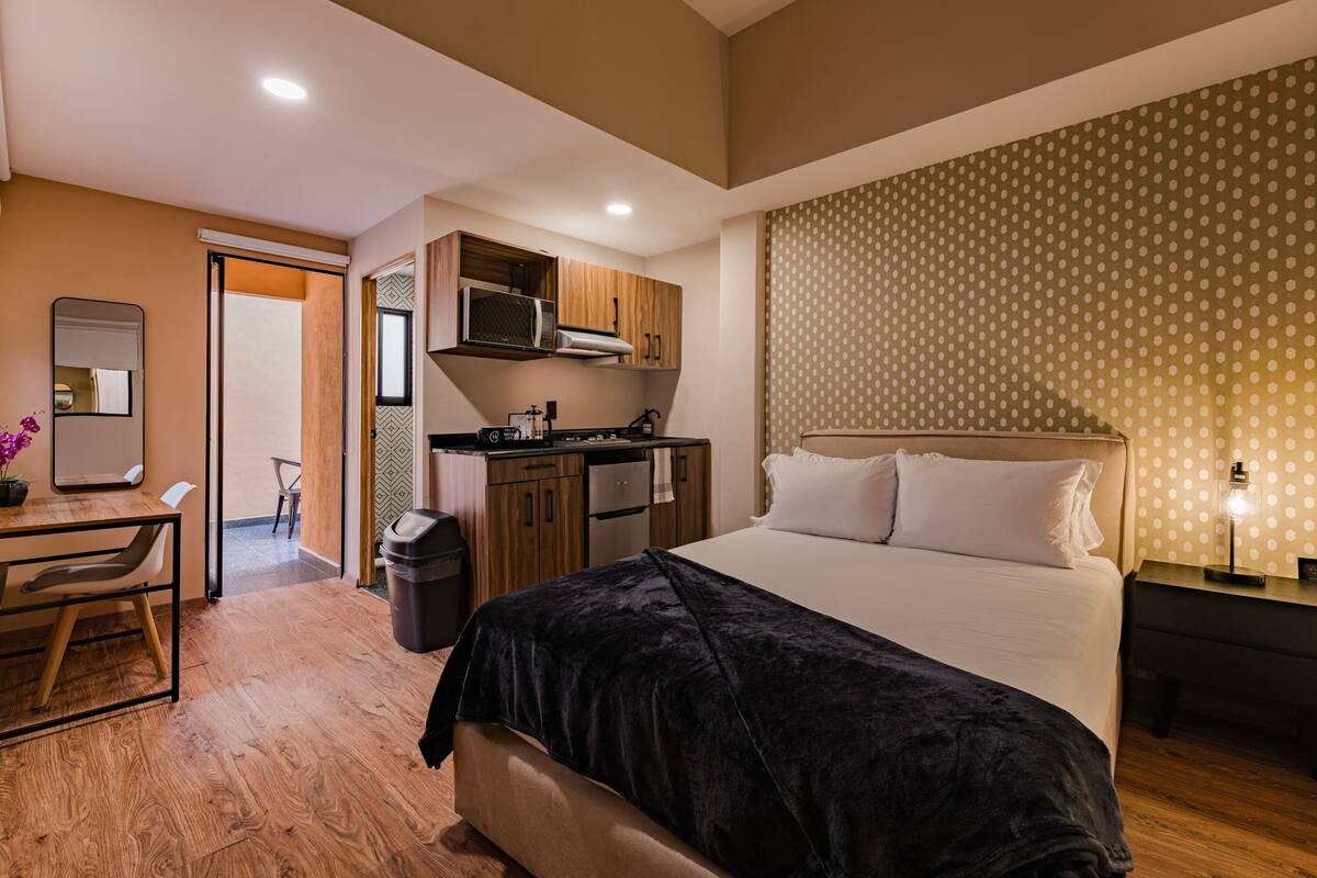 Une chambre d’hôtel équipée d’un lit, d’un bureau, d’un four à micro-ondes et d’une petite kitchenette.