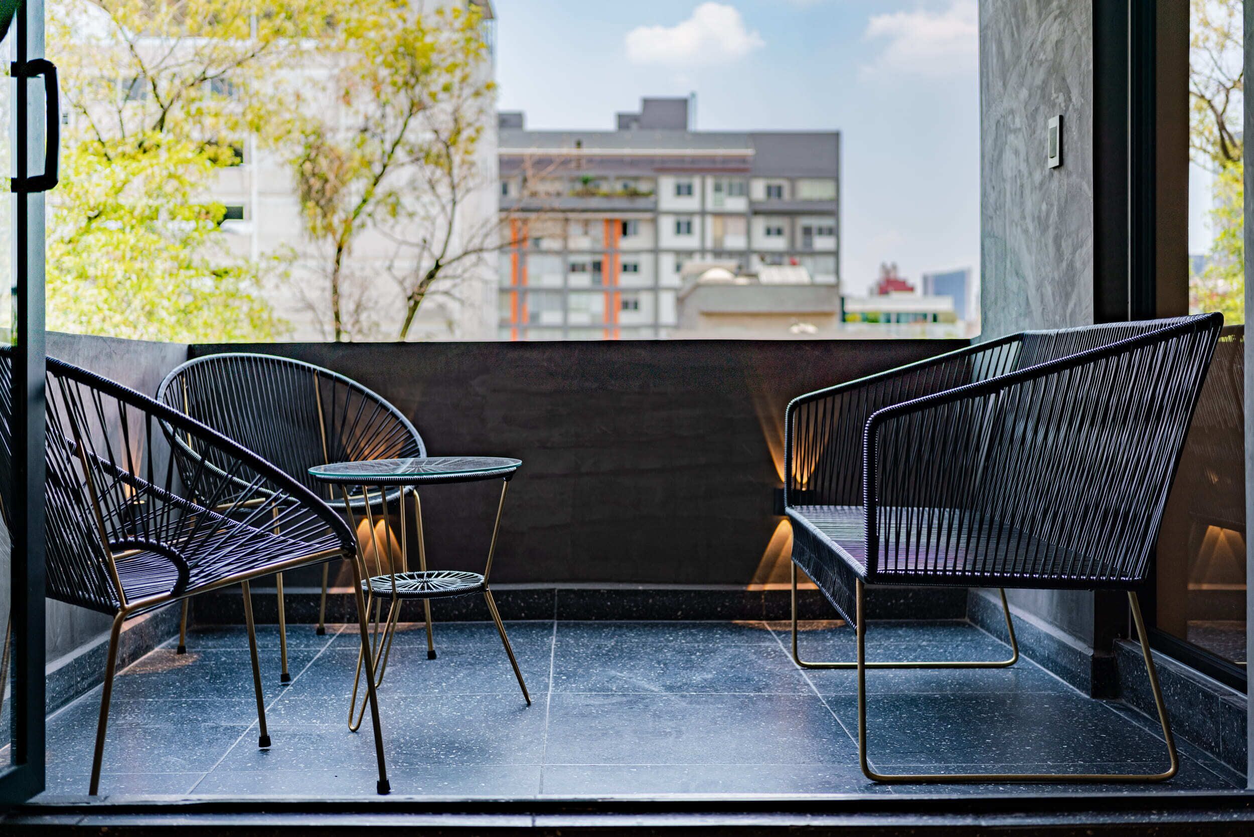 Un balcon avec deux chaises en fil de fer noir et une petite table ronde, donnant sur un paysage urbain.