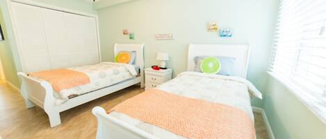 A bedroom with two single beds, a ceiling fan, a nightstand with a lamp, and a window with blinds.