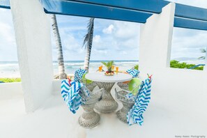 Een ronde tafel met stoelen onder een blauw dak, met uitzicht op de oceaan.
