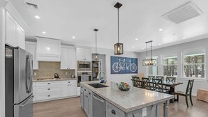 Una cocina moderna con armarios blancos, encimera de granito y un comedor con mesa y sillas.