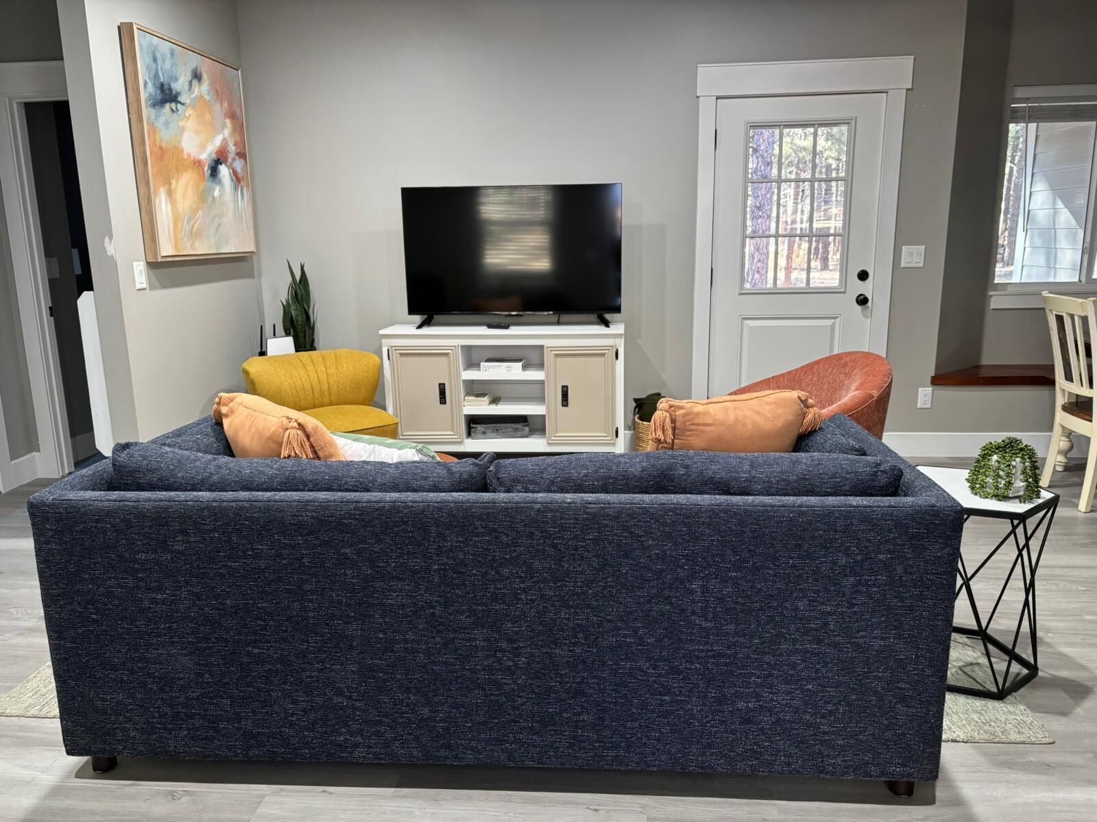 A living room with a dark blue sofa, a yellow armchair, and a television on a white cabinet.