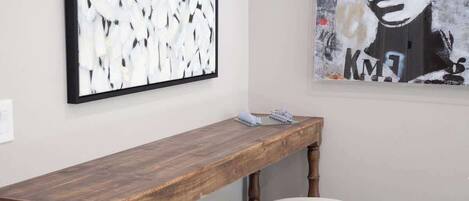 A room with a wooden bench and two stools, a framed abstract painting, and a portrait.