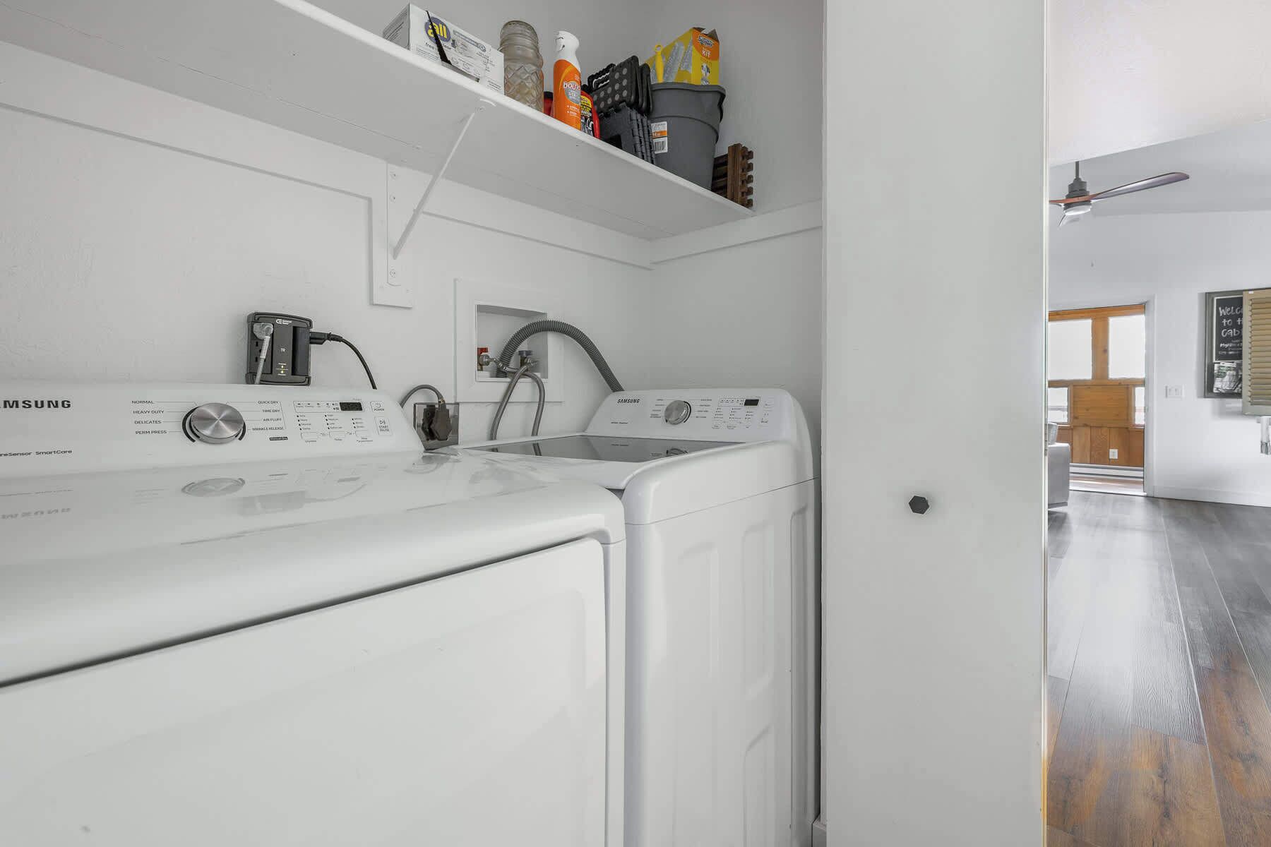 A laundry area with a Samsung washer and dryer, a sink, and a shelf with cleaning supplies.