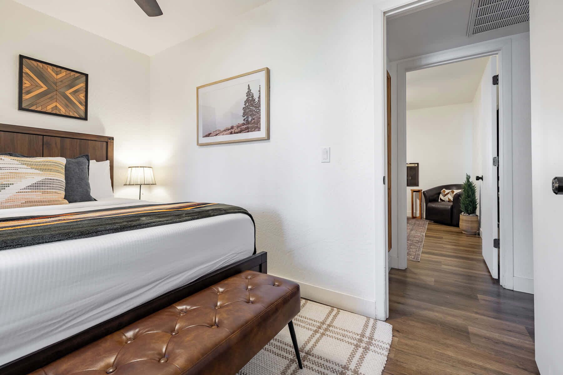 Ein Schlafzimmer mit Bett, Bank, Wandbildern und einem zur anderen Kammer führenden Gang.