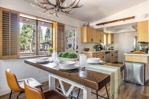 Una cocina con armarios de madera, una mesa de comedor con sillas, una lámpara de araña y vistas al exterior.