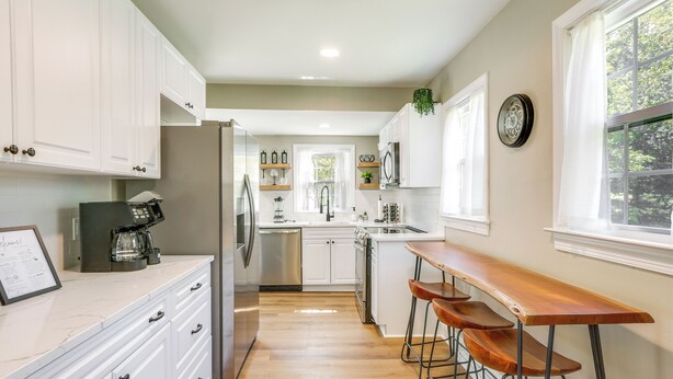 A modern kitchen with white cabinets, a stainless steel refrigerator, a wooden bar counter, and a window with a view of trees. - Charming Greensboro Home - 2 Mi to Downtown! (Greensboro)