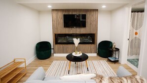 A modern living room with a flat-screen TV mounted on a wooden panel wall, two green armchairs, a black coffee table with decorative items, a grey sofa with a fur throw, and a striped area rug. - Modern 2 bed / 2 bath condo with hot tub. 5 min to Skiing and Main St.! (Park City)