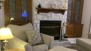 A living room with a stone fireplace, wooden cabinets, a sofa, an ottoman, and a table with a lamp. - Davis Ranch in beautiful Plainview Arkansas next to Nimrod Lake. Pet Friendly. (Plainview)