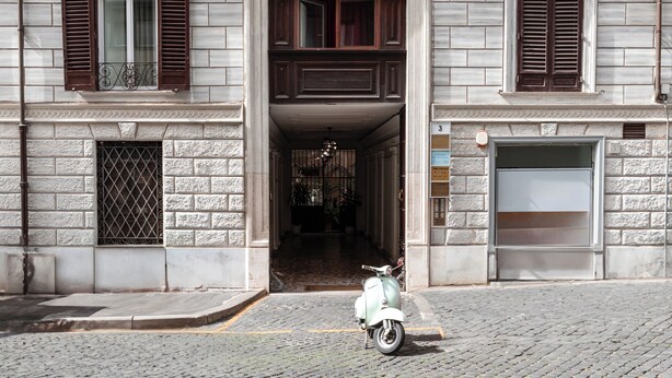 Um edifício com rua de paralelepípedos, uma scooter estacionada e uma porta de garagem.