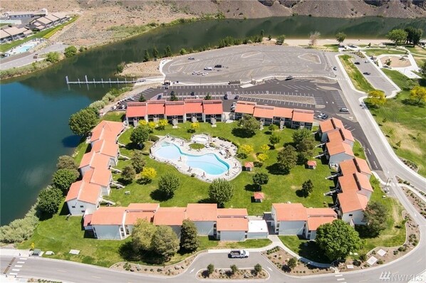 An aerial view of a resort with a central swimming pool, connected buildings, and a parking area.