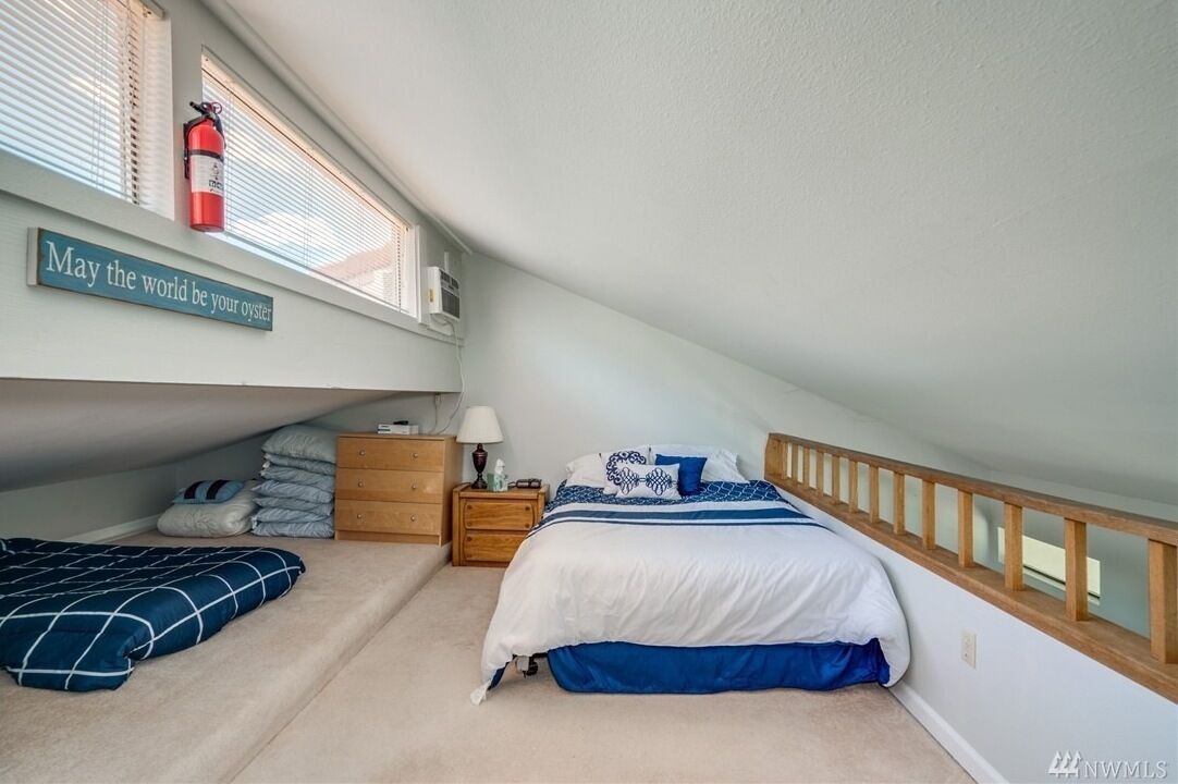 A bedroom with a bunk bed, a bedside table with a lamp, a fire extinguisher on the window sill, and a motivational sign on the wall.