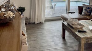 A room with a wooden floor, a white sofa, a coffee table, and a view of the ocean through large sliding glass doors. - Renovated, direct oceanfront 5BR/6BA private pool home sleeps 16. (New Smyrna Beach)