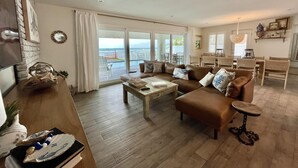 A spacious living room with a large sofa, a coffee table, and a dining area with wicker chairs. - Renovated, direct oceanfront 5BR/6BA private pool home sleeps 16. (New Smyrna Beach)