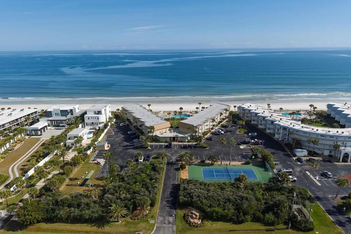 Un hotel frente al mar con vista a la playa, varias piscinas y una cancha de tenis.