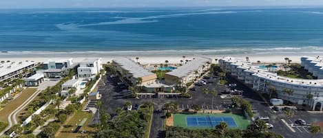 Un hotel frente al mar con vista a la playa, varias piscinas y una cancha de tenis.
