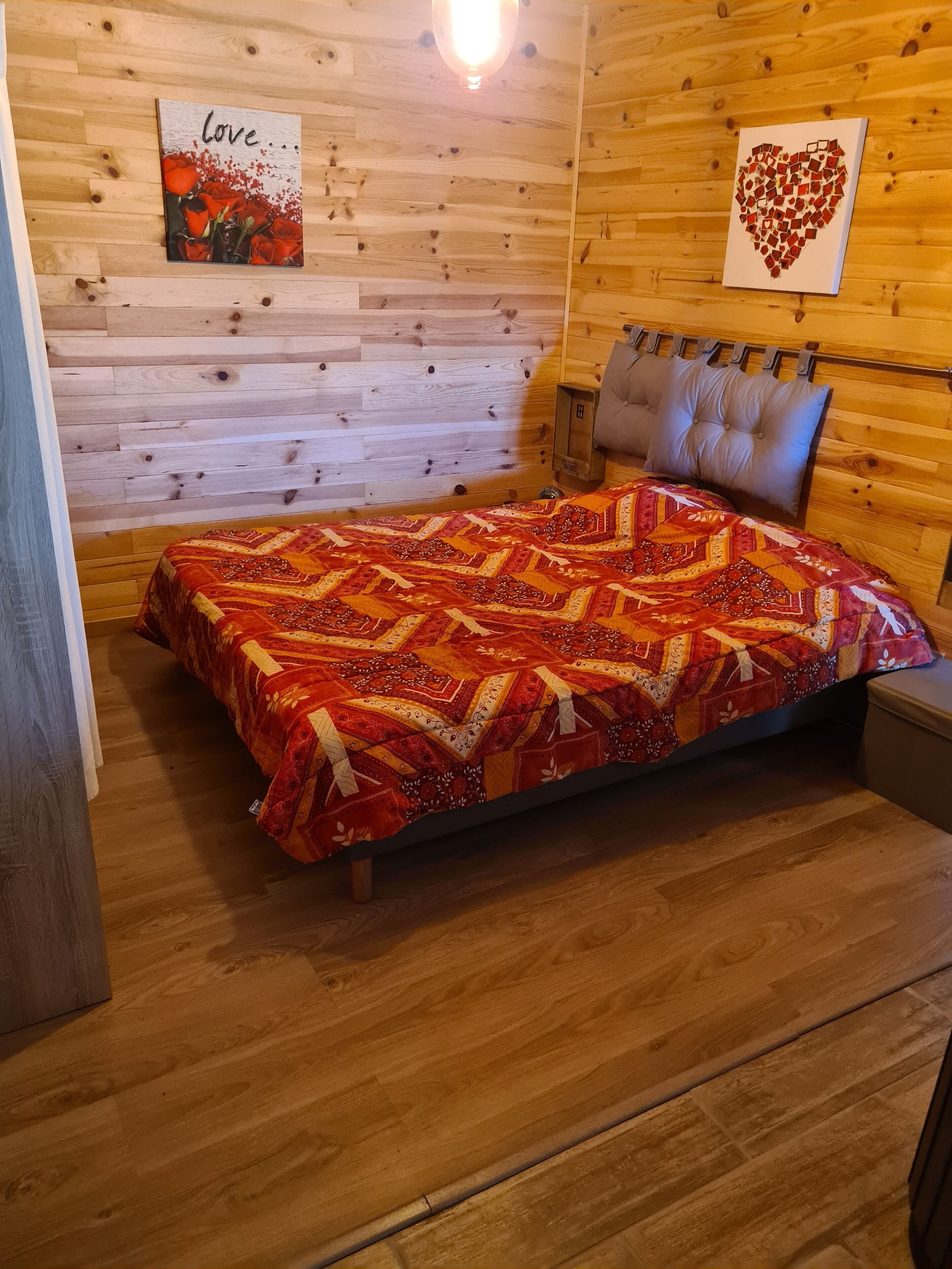Um quarto de madeira aconchegante, com uma cama, uma parede com o letreiro 'Love...' e uma foto em formato de coração.