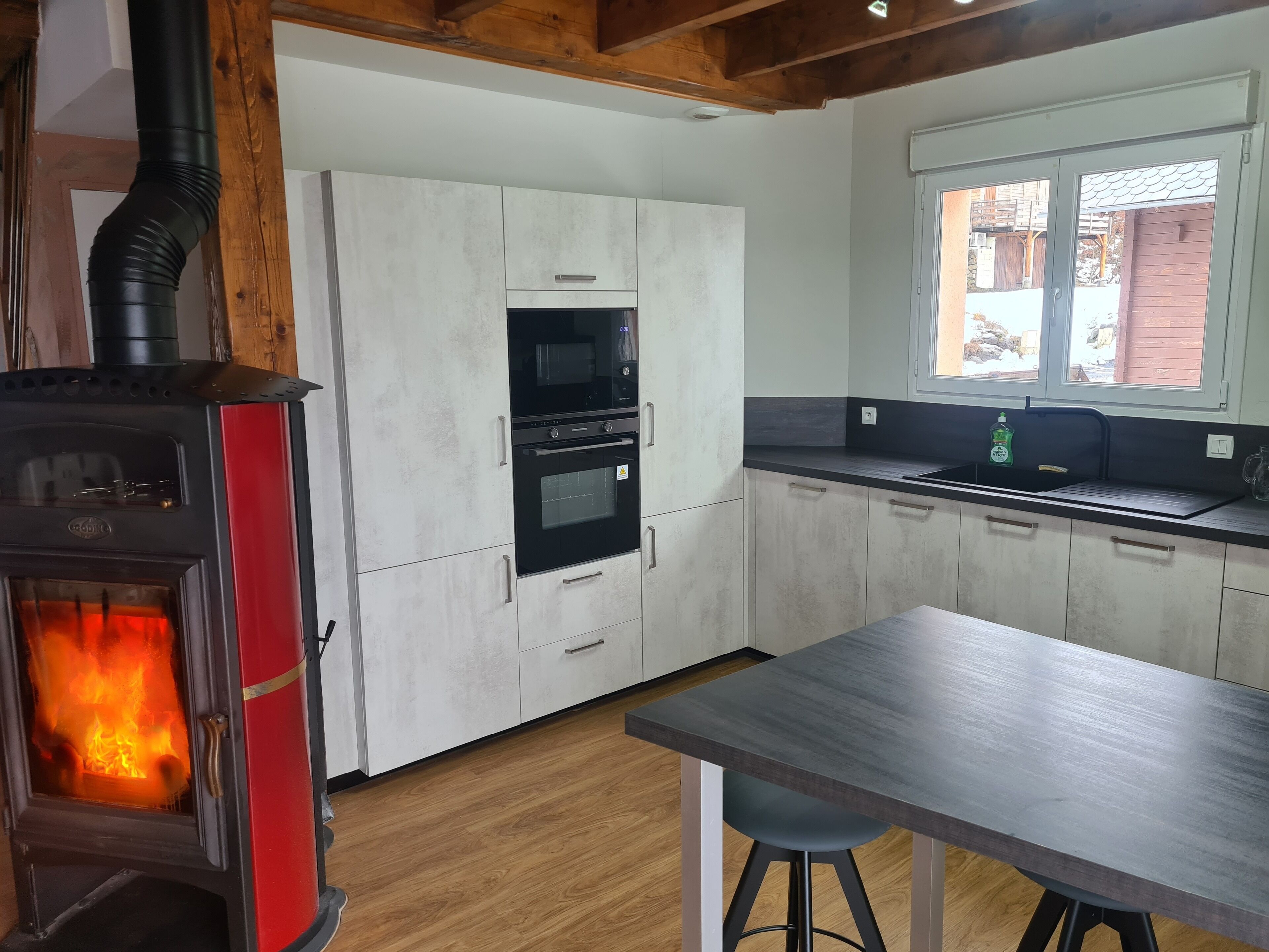 Una cocina moderna con estufa de leña, horno empotrado, microondas y ventana con vistas al exterior.