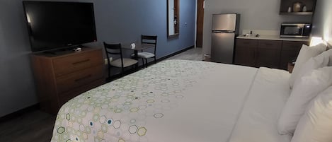 Habitación de hotel con cama, televisión, escritorio con sillas, refrigerador y microondas.