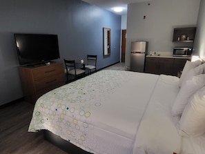 Hotellihuone, jossa on sänky, televisio, työpöytä tuoleineen, jääkaappi ja mikroaaltouuni.