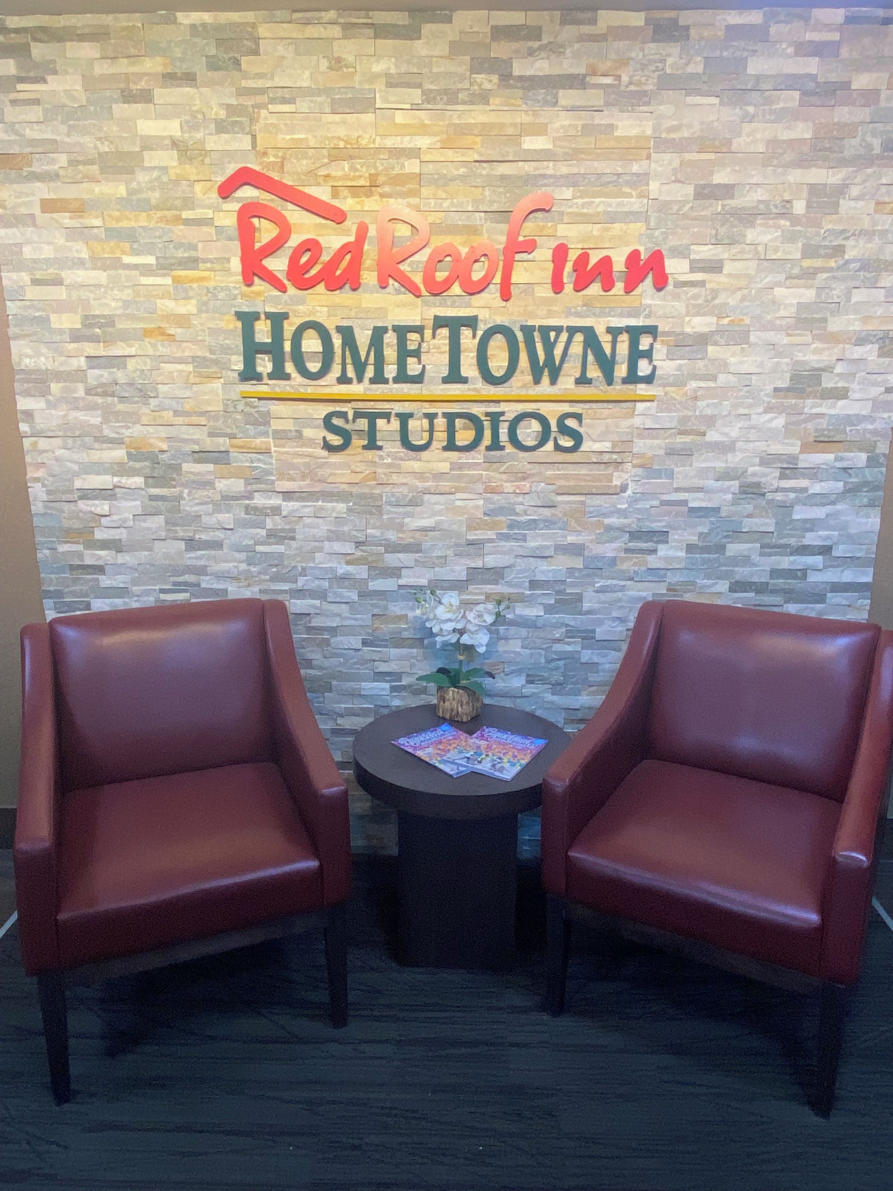 Un Red Roof Inn Hometown Studios con un fondo de pared de piedra, dos sillones de cuero y una mesita con revistas.