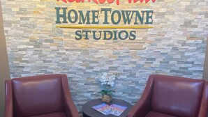 A Red Roof Inn Hometown Studios with a stone wall backdrop, two leather armchairs, and a small table with magazines. - HomeTowne Studios by Red Roof Prattville (Prattville)