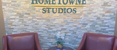 A Red Roof Inn Hometown Studios with a stone wall backdrop, two leather armchairs, and a small table with magazines.