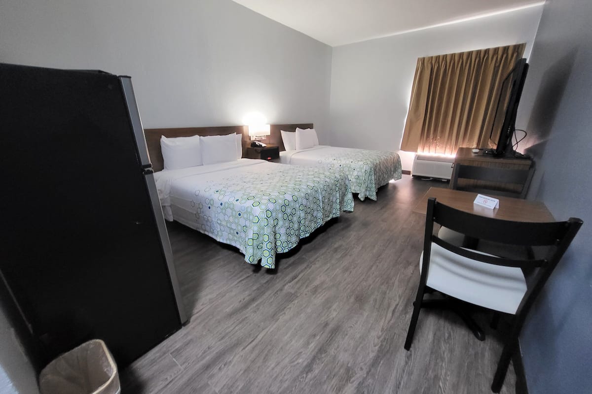 Een hotelkamer met twee bedden, een bureau, een stoel, een televisie en een prullenbak.