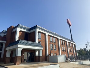 A modern building with a brick facade, large windows, and a prominent flagpole. - HomeTowne Studios by Red Roof Prattville (Prattville)