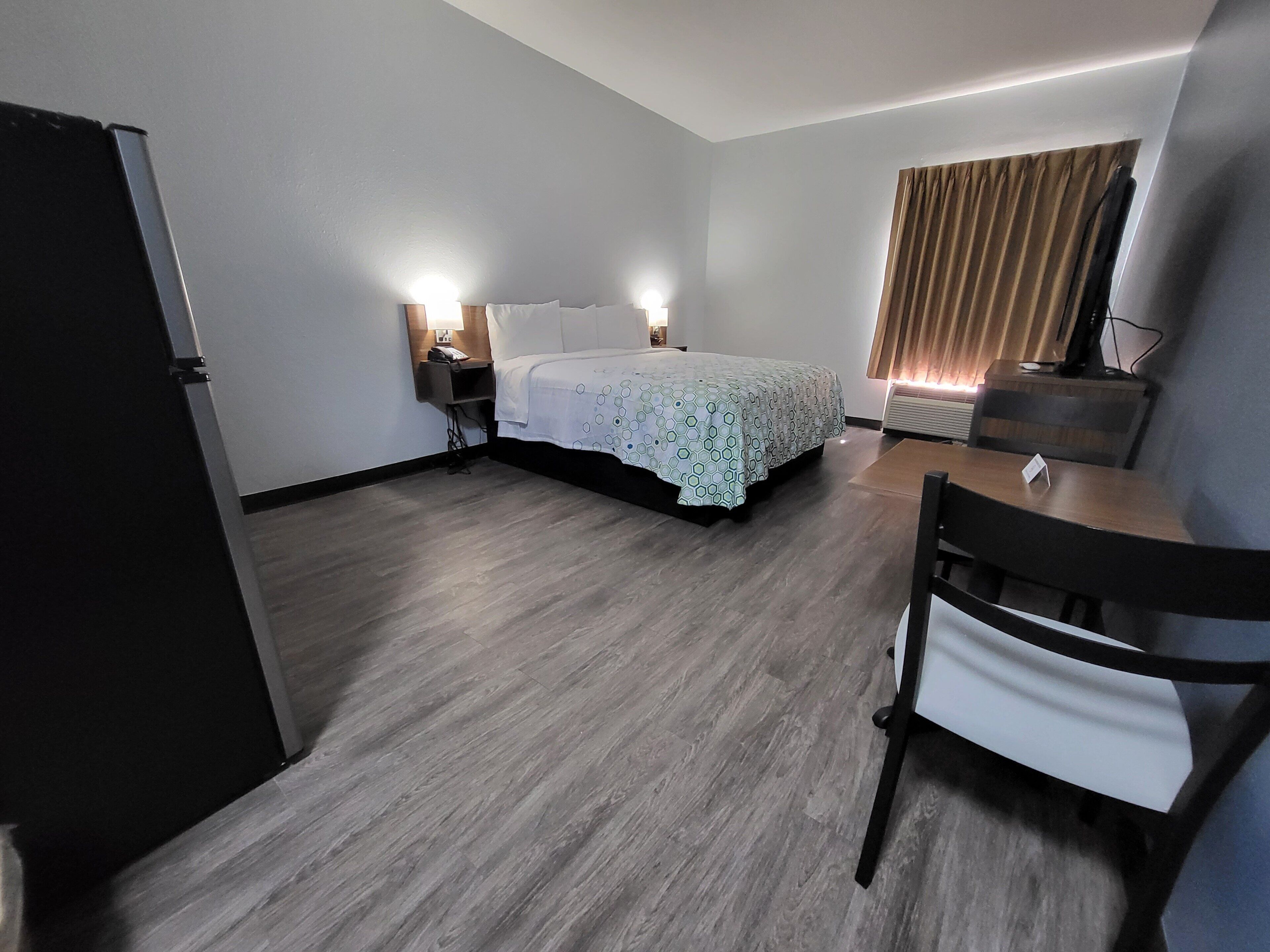 A hotel room with a bed, bedside lamps, a desk with a chair, and a television.