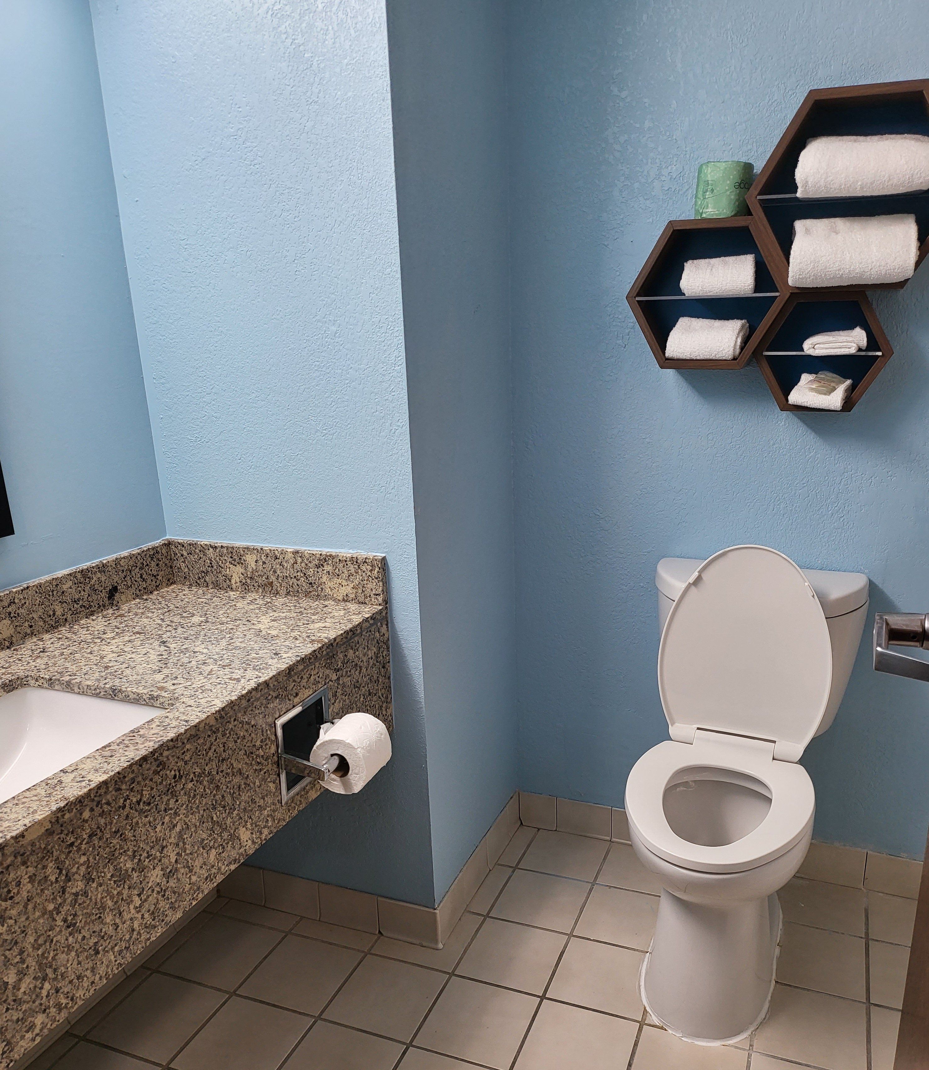 A bathroom with a granite countertop sink, a toilet, and a towel rack with folded towels.