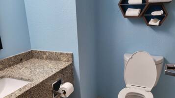 A bathroom with a granite countertop sink, a toilet, and a towel rack with folded towels.