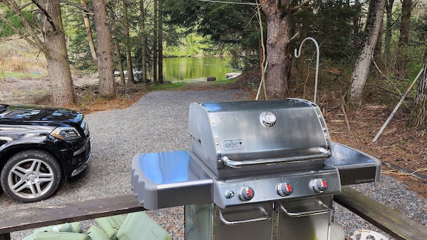 En sort bil parkeret ved en træterrasse med en Weber Genesis grill.
