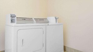 A front-loading washing machine in a laundry room with a tiled floor and plain walls. - Deluxe Double Room with Two Double Beds - Non-Smoking (Roanoke)