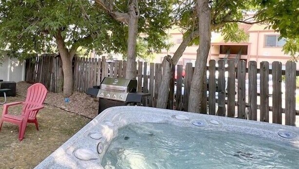 Un jacuzzi en un patio trasero con cerca de madera, una parrilla y una silla roja.