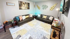 Una sala de estar con dos sofás, una mesa de centro, un tapete, un televisor montado en la pared y objetos decorativos.