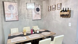 Un comedor con una mesa larga, sillas blancas y una obra de arte abstracta en la pared.