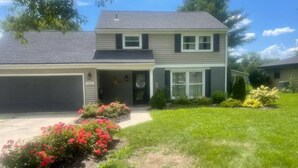 A two-story house with a garage, a front porch, and a well-maintained lawn with flowering plants. - The Family and Friends Home
 (New Haven)
