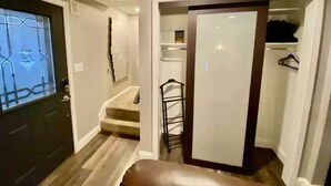 A hallway with a dark door, a staircase, and a closet with a mirror and shelves. - The Family and Friends Home
 (New Haven)