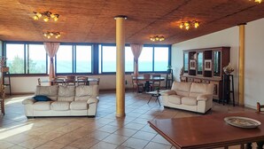 A spacious living room with two sofas, a wooden coffee table, and a dining area with a table and chairs. Large windows offer a view of the sea. - Lovely home in Caronia (Caronia)